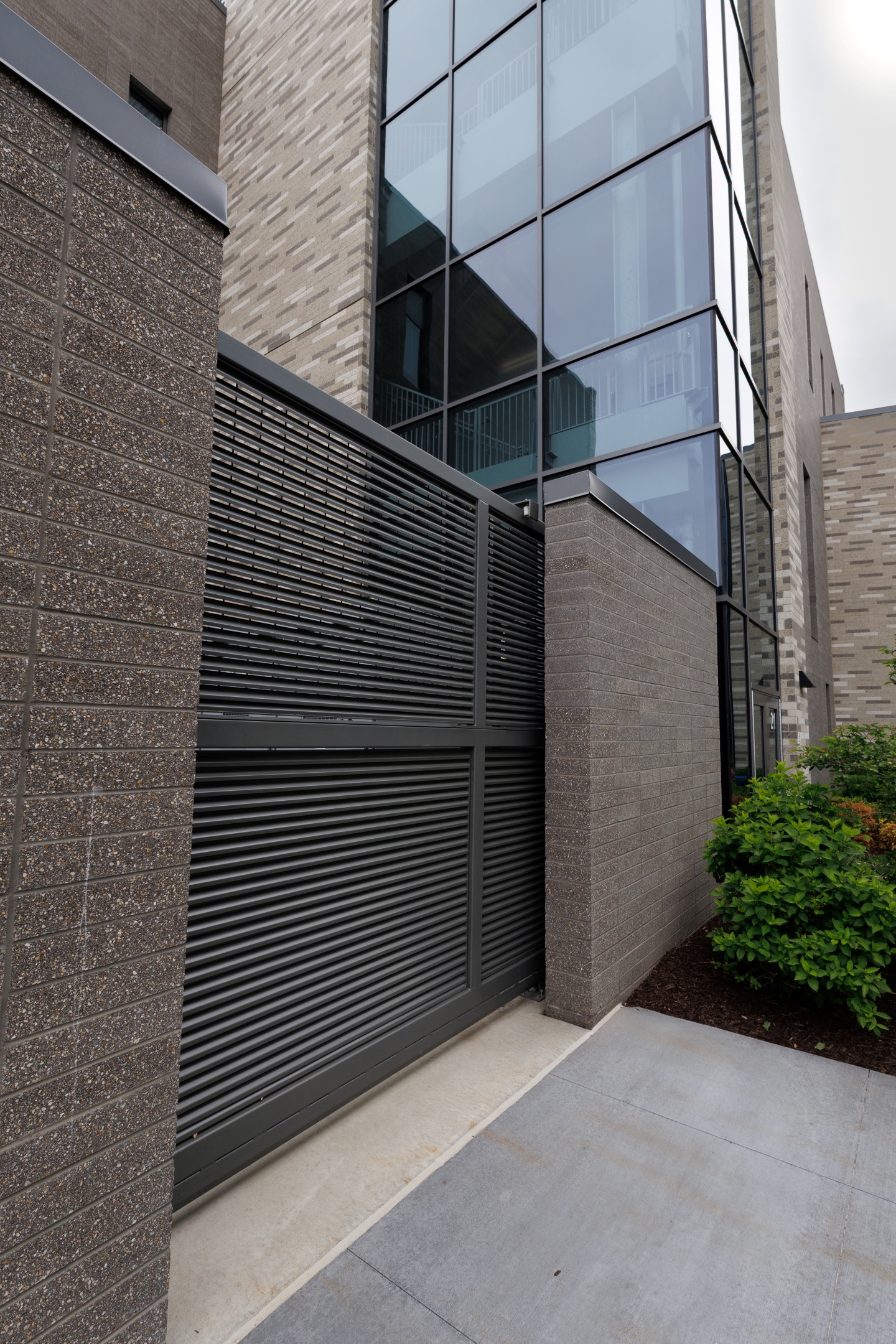 A decorative metal gate, featuring architectural steel louvers, concealing a mechanical yard enclosure at a hospital.